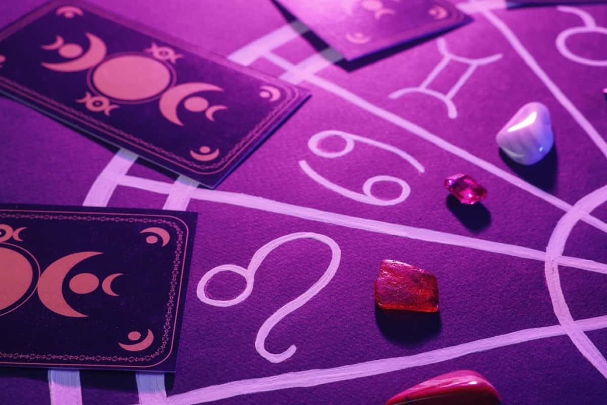 Natural stones for zodiac signs, tarot cards and drawn astrology chart on purple background, closeup. Color tone effect