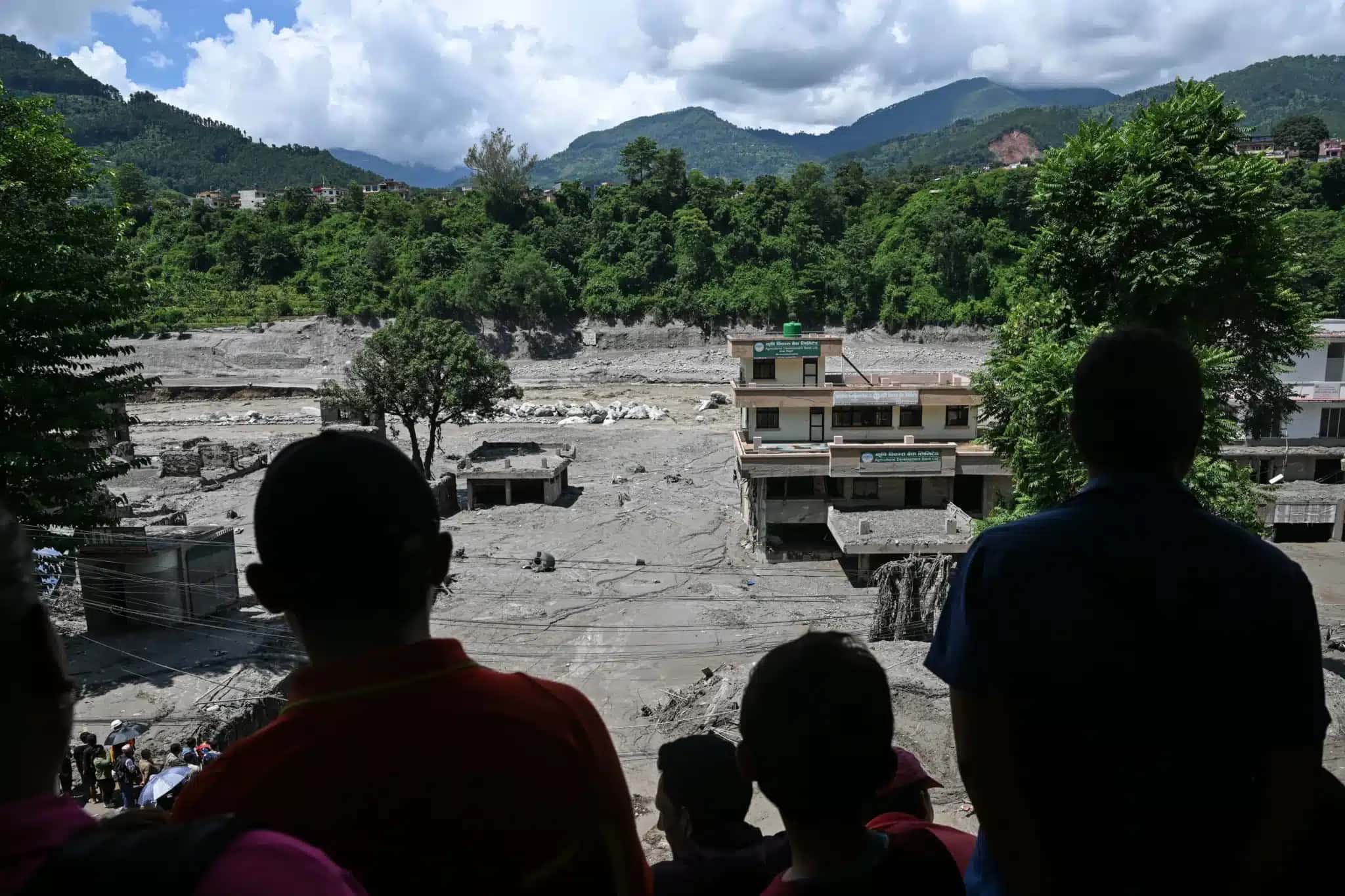 Pessoas em um telhado observam os danos causados ​​por enchentes repentinas em Trishuli, Nepal, na quinta-feira, 27 de agosto.