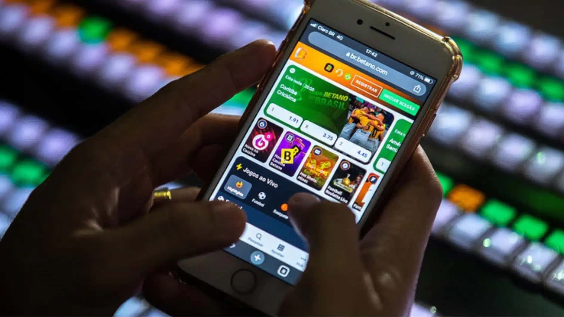 Mão segurando um celular cuja tela exibe um aplicativo de cassino online