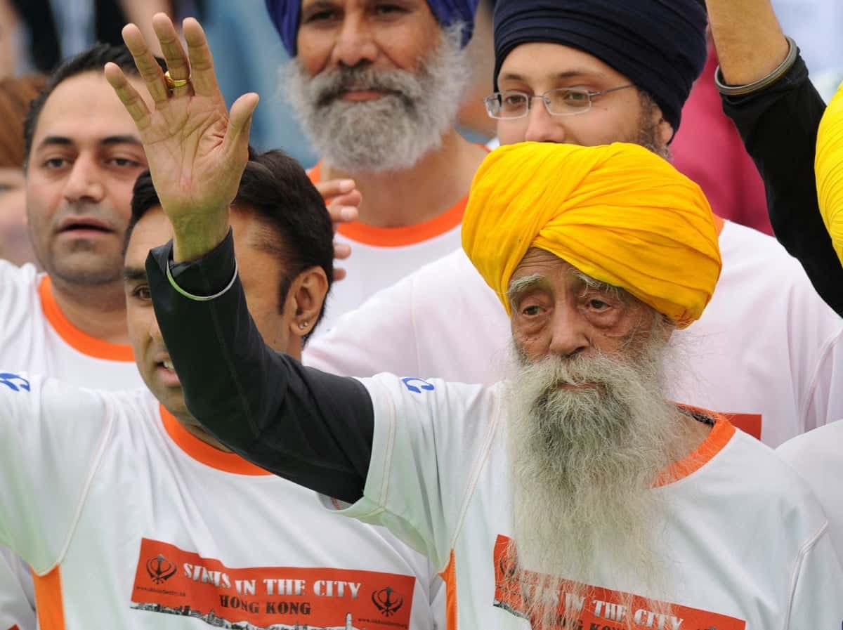 (FILES) Indian-born British national Fauja Singh (R) waves to the media after crossing the finish line in the 10-km event as part of the Hong Kong Marathon on February 24, 2013. India's Fauja Singh, believed to be the world's oldest distance runner, has died in a road accident aged 114, his biographer said on July 15, 2025. (Photo by Dale DE LA REY / AFP)