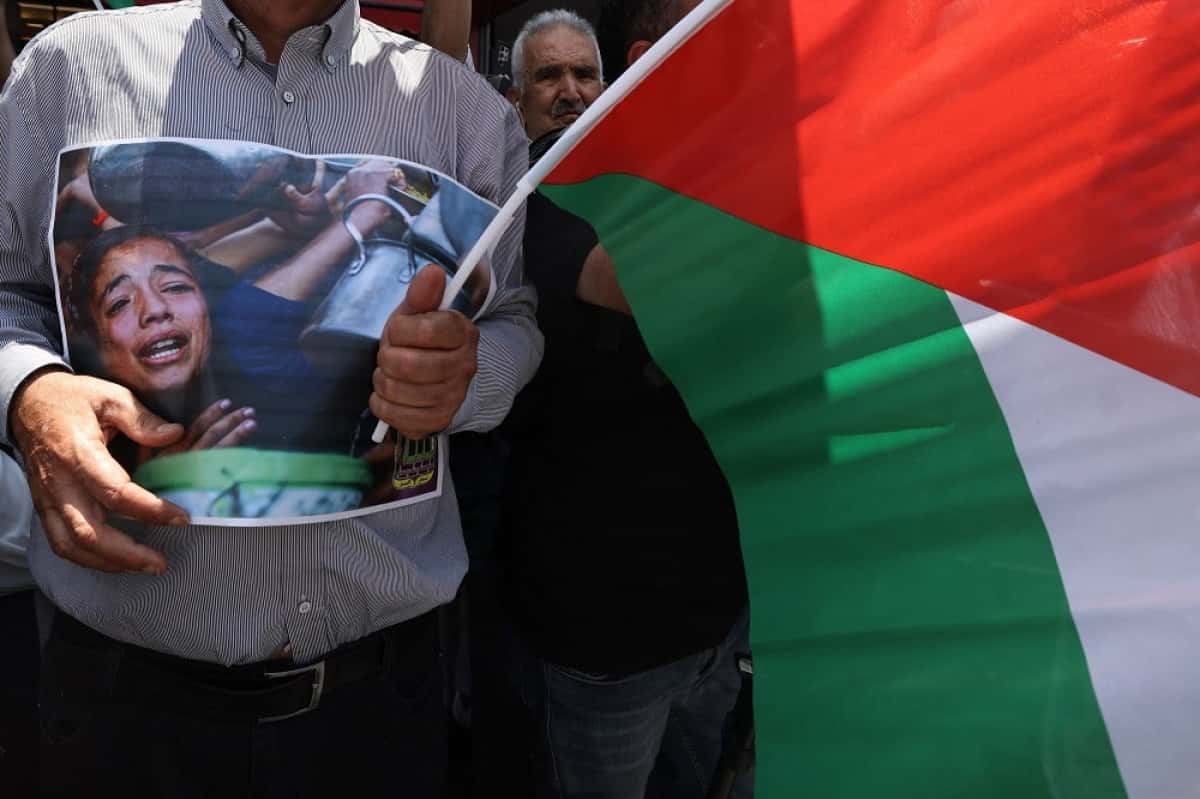 A Palestinian man carries a placard and waves the national flag during a demonstration in support of palestinians in Gaza facing severe shortages of food and other essentials, in the city of Nablus, in the Israeli occupied West Bank on July 22, 2025. The head of Gaza's largest hospital on July 22 said 21 children have died due to malnutrition and starvation in the Palestinian territory in the past three days, amid a devastating assault by Israeli forces. (Photo by JAAFAR ASHTIYEH / AFP)