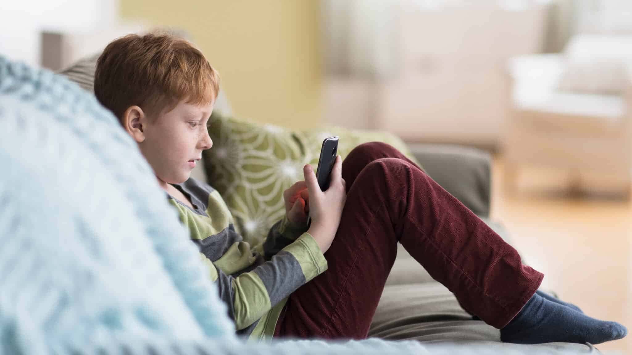 USA, New Jersey, Boy (6-7) sitting on couch and using cell phone