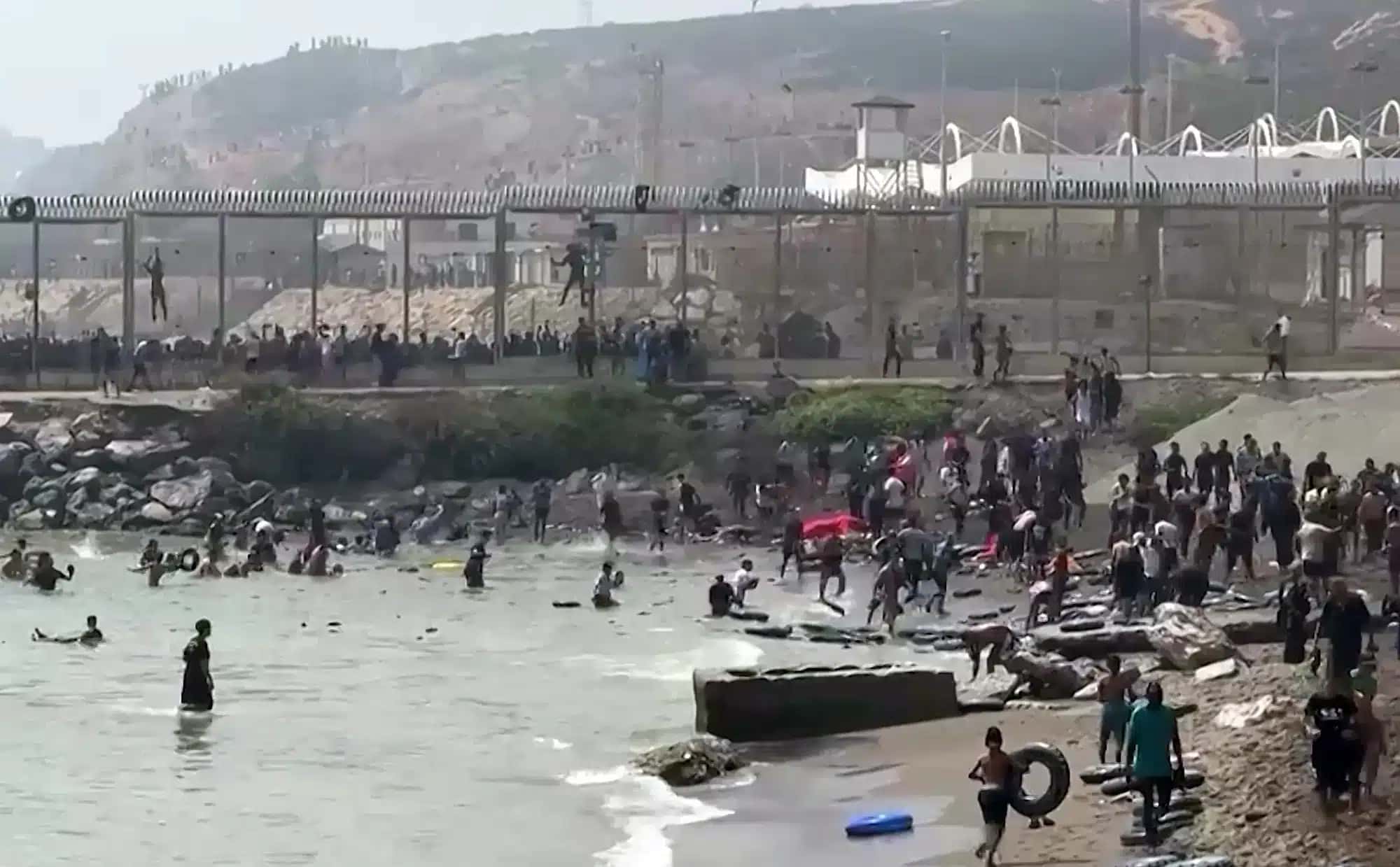 This video frame grab obtained from an AFP video shows migrants reaching the shore of Spanish north African exclave of Ceuta, after swimming around the border fence between Morocco and Spain, in Ceuta on July 30, 2026. Hundreds of migrants entered the Spanish north African exclave of Ceuta today, AFP reporters saw, many of them having swum by sea around the frontier fence. Migration from Morocco into Spain's two north African territories, Ceuta and Melilla, has long been a politically sensitive issue between the two countries, as thousands cross the border at times. AFP reporters saw a stream of adults and children, most of them wet, entering the town. (Photo by Lucía DIAZ / AFP)