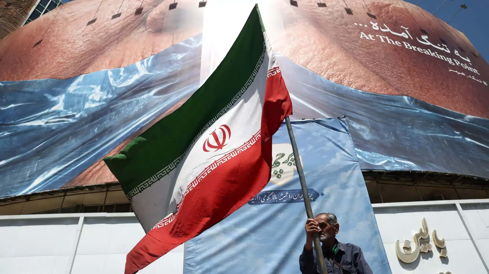 Homem segura bandeira iraniana perto de outdoor anti-EUA representando o presidente dos EUA, Donald Trump, e o Estreito de Ormuz, em Teerã, Irã, em 30 de maio de 2026