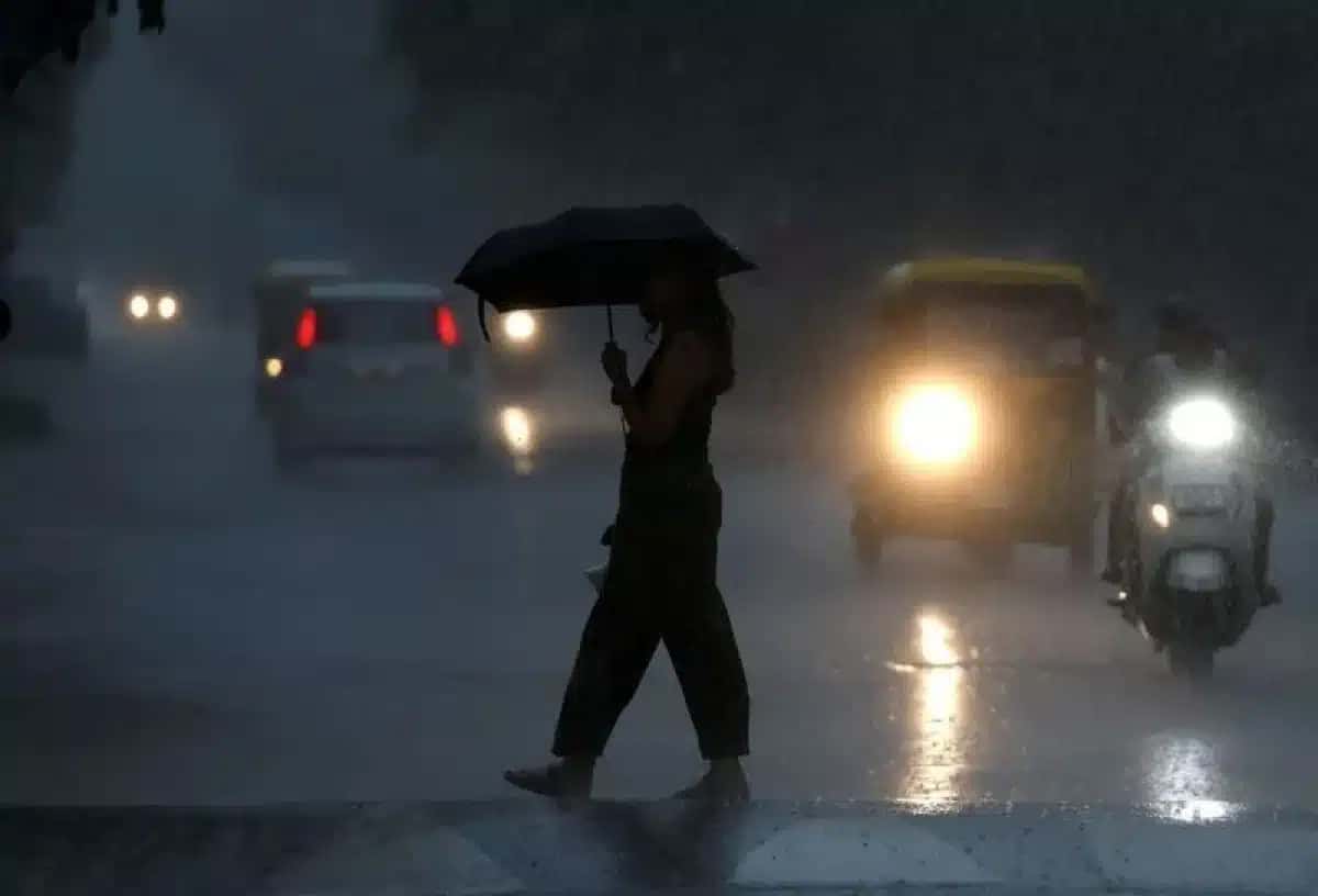 Uma mulher segurando um guarda-chuva atravessa uma rua durante uma forte chuva de monção, enquanto veículos circulam em condições de baixa visibilidade em Ahmedabad