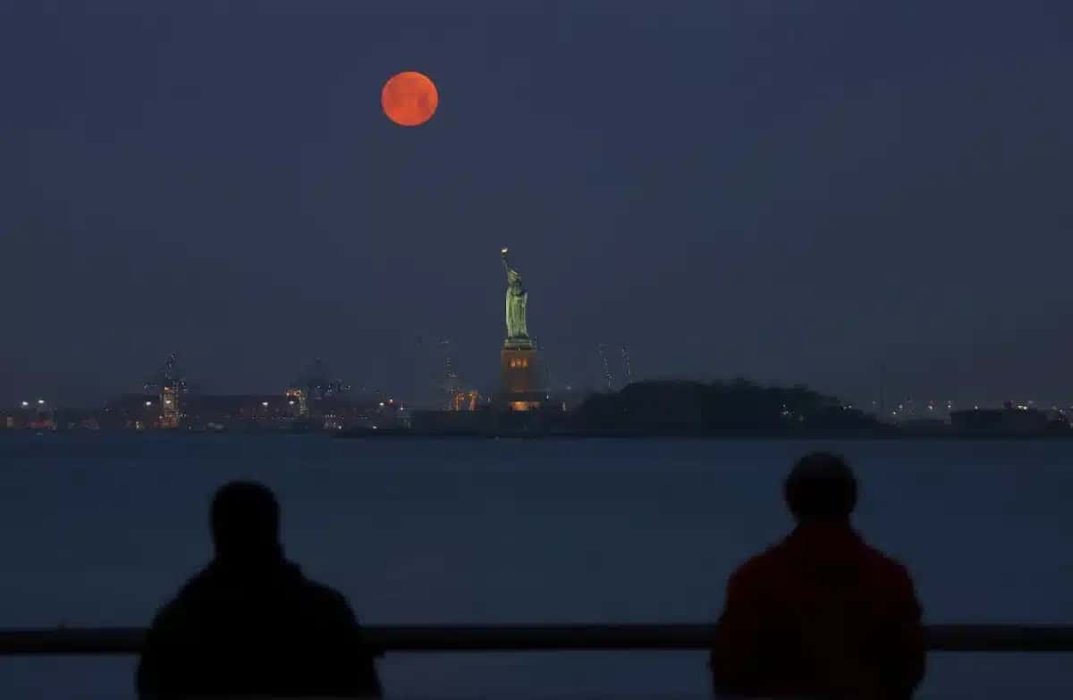 Dois pescadores observam a superlua atrás da Estátua da Liberdade, em Nova York