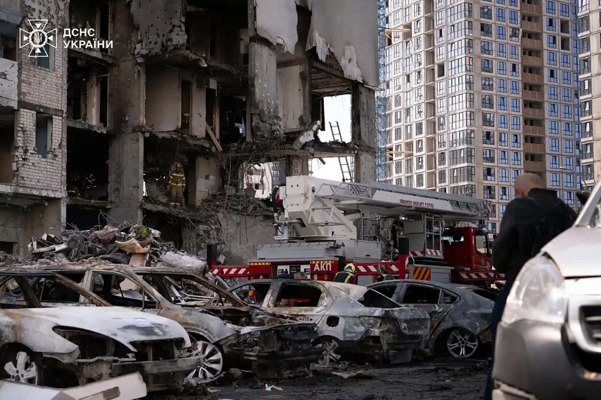 Carros queimados estacionados em frente a um edifício parcialmente destruído por um ataque de mísseis russos à capital ucraniana, Kiev