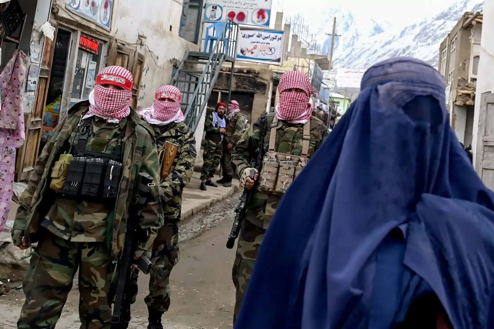 Agentes de segurança do Talibã montam guarda enquanto uma mulher afegã caminha pela rua de um mercado no distrito de Baharak, na província de Badakhshan, Afeganistão, em 26 de fevereiro de 2024.