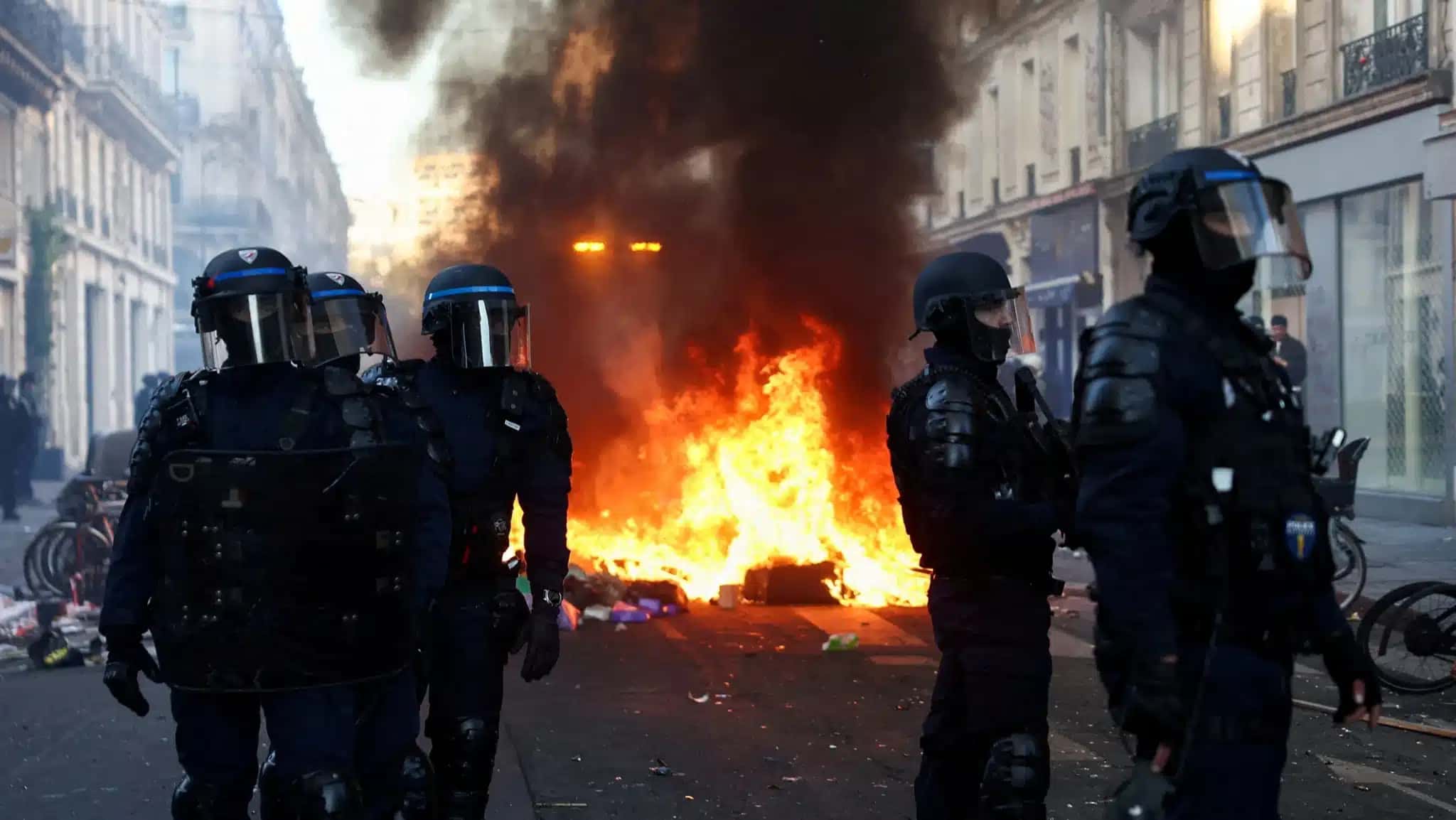 Incêndio consome objetos, enquanto policiais fazem a guarda durante distúrbios civis em Paris, França.